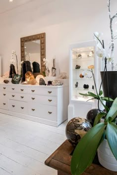 a bedroom with white furniture and lots of shoes on the dresser next to a plant