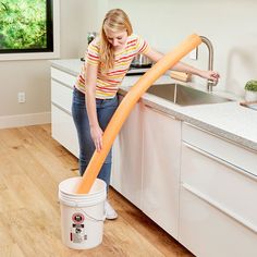 a woman is cleaning the kitchen with a bucket and orange hose in front of her