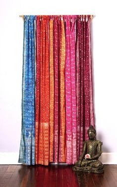 a buddha statue sitting in front of a curtain that is colored red, blue and orange