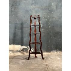 a tall wooden shelf with glass shelves on it's sides in front of a concrete wall