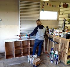 a man standing in front of a wooden cabinet filled with paint cans and other items