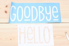 two stickers that say goodbye and hello on wooden surface with scissors, paper clips and pen