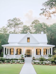 a white house with black shutters and flowers on the front lawn in front of it