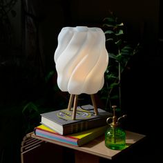 a white lamp sitting on top of a wooden table next to a stack of books