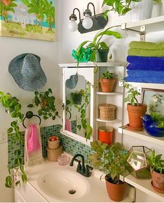 a bathroom sink with plants and towels on the shelf next to it in front of a mirror