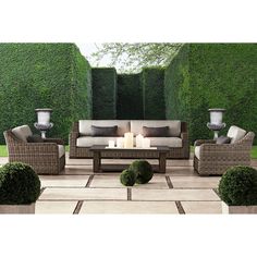 an outdoor living area with couches, chairs and candles on the table in front of green hedges