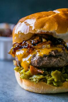 a cheeseburger with meat, onions and guacamole on a bun