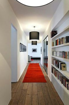 a long hallway with bookshelves and a red rug