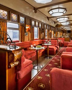 the inside of a train car with red couches and tables on each side of it