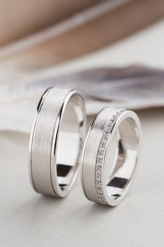 two white gold wedding bands with diamonds on them, sitting next to each other in front of a magazine