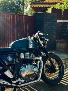 a black motorcycle parked in front of a wooden fence on a sunny day with no one around