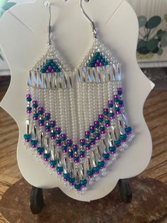 a pair of beaded earrings sitting on top of a wooden table next to a white plate