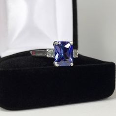 Beautiful Tanzanite* & White Sapphire Ring * 2.25ct Emerald Cut Violet Blue Tanzanite* measures 9mm x 7mm * 3.5mm Brilliant Cut White Sapphire Accents * 2.5cts Total weight * 14k White Gold * Size 9 Hallmarked & Gift Ready! Matching Earrings & Pendant Necklace is also Available! *Tanzanite is one of very few gemstones that cannot be grown in a Lab, however, these Laboratory Grown Simulate Stones are optically identical to a natural Tanzanite in color and are just as hard but, do not Sapphire Necklace Pendants, Trending Jewelry, White Sapphire Ring, Gifts For Fiance, Fine Art Jewelry, Tanzanite Ring, Blue Tanzanite, Natural Tanzanite, Sapphire Necklace