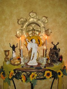 a table with sunflowers and candles on it in front of a gold wall