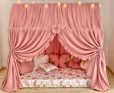 a canopy bed with pink curtains and pillows on top of it, in a room that has hardwood floors