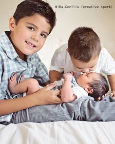 two young boys laying on top of a bed next to each other holding their babies