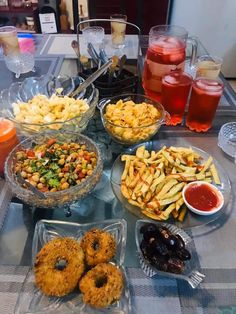 an assortment of food is displayed on a table with drinks and condiments in bowls