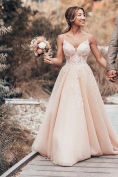 a bride and groom holding hands walking down a wooden walkway in their wedding gowns