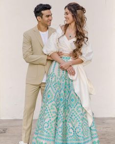 two people standing next to each other in front of a white wall wearing formal clothing