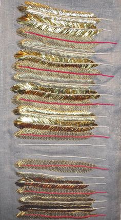 several different types of feathers are arranged on a piece of fabric with red and gold thread