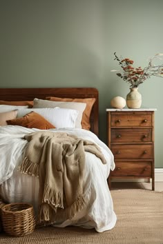 a bedroom with green walls and white linens on the bedspread, brown throw pillows, and a wicker basket