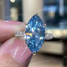 a person holding a blue ring with diamonds on it's sides and an oval shaped diamond