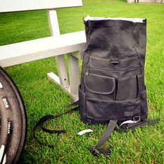 a back pack sitting on the grass next to a white bench with a bike tire