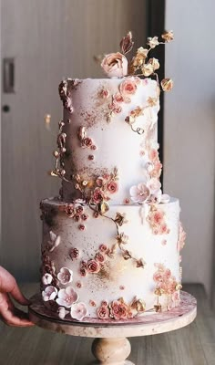 a white and pink wedding cake with flowers on it is being held by a person