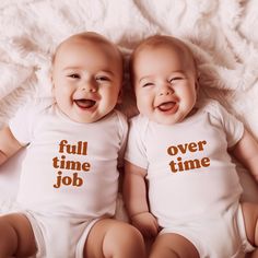 two baby babies laying next to each other on a white blanket smiling at the camera