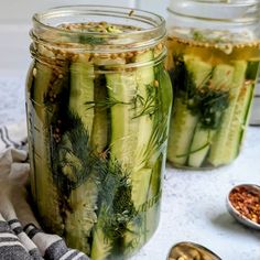 two jars filled with pickled cucumbers next to bowls of nuts and herbs