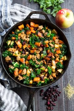 a skillet filled with meat, vegetables and cranberries next to an apple