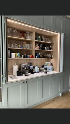 a kitchen with gray cabinets and shelves filled with glasses, coffee maker and other items