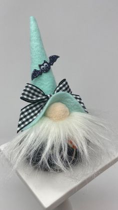 a small green gnome with white hair and a bow on it's head sitting on a shelf