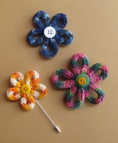 three crocheted flower pins are shown on a brown surface with a white button