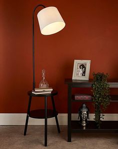 a lamp on a table in front of a red wall and a black end table