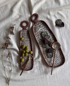 two serving trays filled with olives on top of a white cloth covered bed