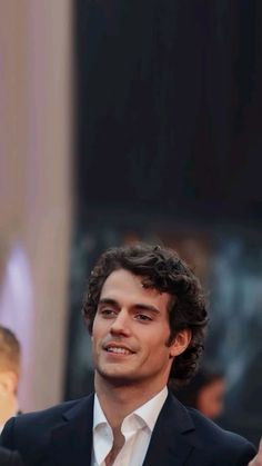 a man in a black suit and white shirt is talking to the crowd at an event