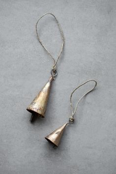 two small bells hanging from a string on a gray surface, one has a silver chain and the other is a bronze bell