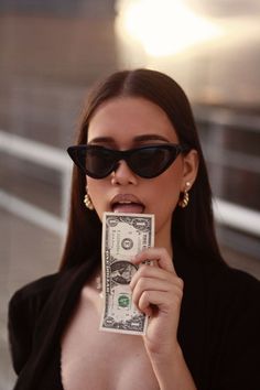 a woman in sunglasses holding up a dollar bill