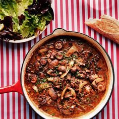 a pot of stew with mushrooms in it next to a plate of bread and salad