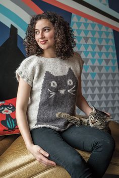 a woman sitting on a couch with a cat in her lap and smiling at the camera