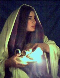 a woman in a white robe holding a lit candle and looking at the light coming from her hands