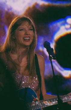 a woman singing into a microphone while holding a guitar