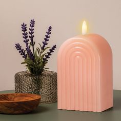 a pink candle sitting on top of a table next to a wooden bowl and vase