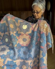 an older woman is holding up a quilt