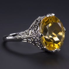 This beautiful and unique solitaire ring features a 4.75ct oval cut citrine set in a classically elegant vintage style design that will never go out of style! Measuring approximately 12mm across, the citrine has a substantial look and a gorgeous sunny yellow hue. Utterly classic and romantic, the antique style setting is richly textured with intricate engraving and graceful filigree. The effect is chic but also dreamy and softly feminine, a perfect choice for a timeless gift or a treat for yours Elegant Yellow Topaz Ring Round Cut, Elegant Yellow Topaz Ring With Round Cut, Elegant Yellow Round Cut Topaz Ring, Elegant Citrine Solitaire Ring, Elegant Solitaire Citrine Ring, Formal Oval Yellow Topaz Ring, Formal Yellow Oval Topaz Ring, Formal Citrine Diamond-cut Ring, Formal Citrine Diamond Cut Ring