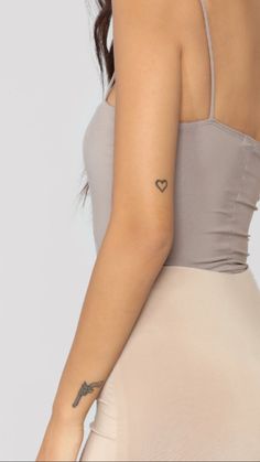 a woman with a small heart tattoo on her left arm, wearing a beige dress