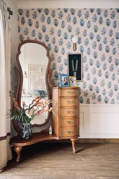 a dresser and mirror in a room with floral wallpaper