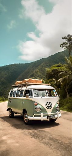 an old vw bus with surfboards on the roof driving down a dirt road