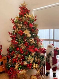 a christmas tree decorated with red and gold ornaments, santa claus standing next to it